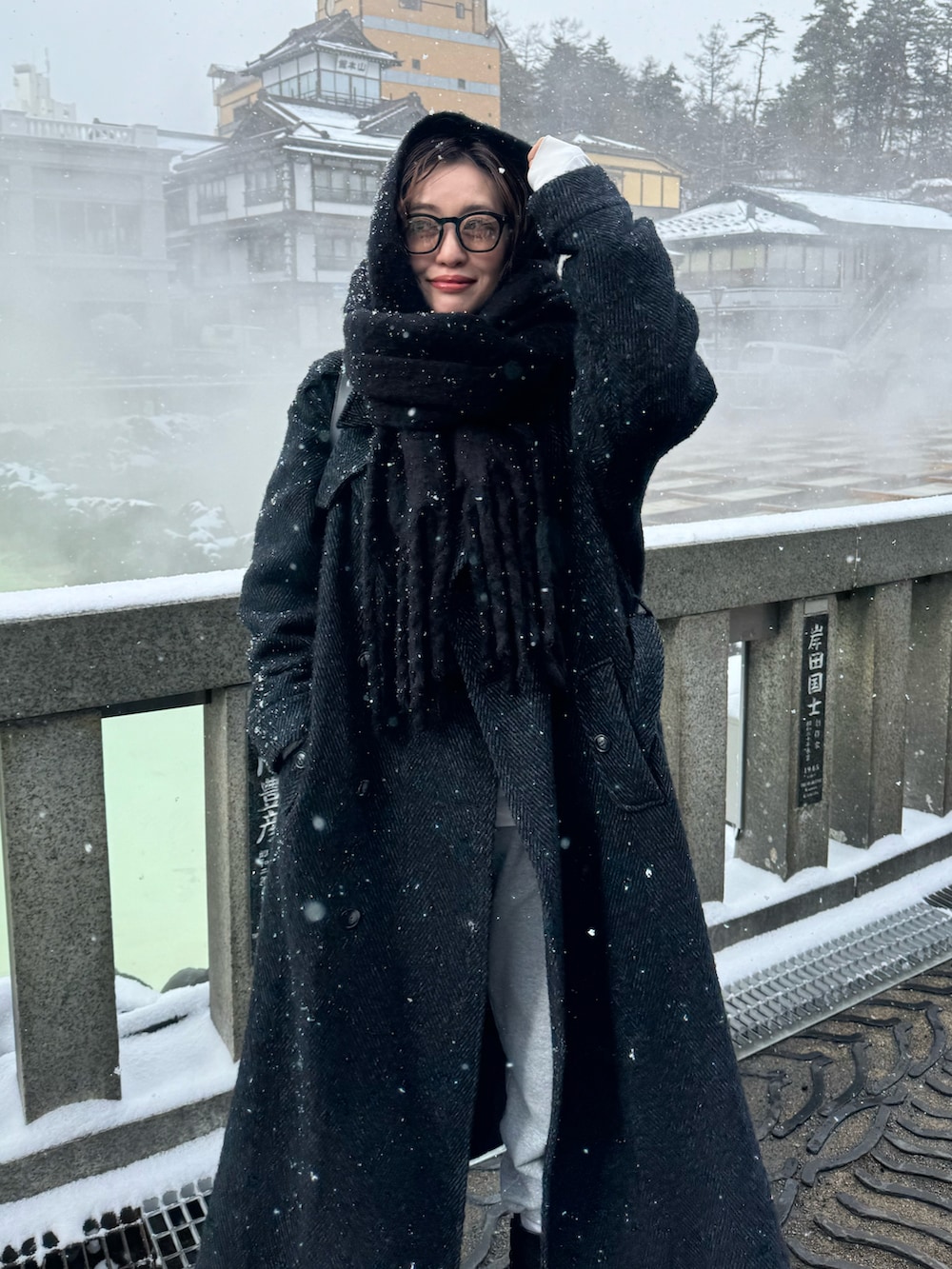 ブラック系のチェスターコート、ブラック系のブーツ、ホワイト系のニット/セーターを着用したレディースの冬コーディネートの2枚目の写真