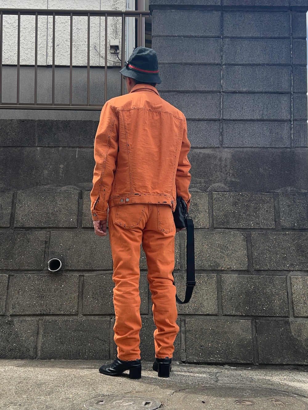 オレンジ系のデニムパンツ、ブラック系のブーツ、ブラック系のショルダーバッグを着用したメンズの春コーディネートの2枚目の写真