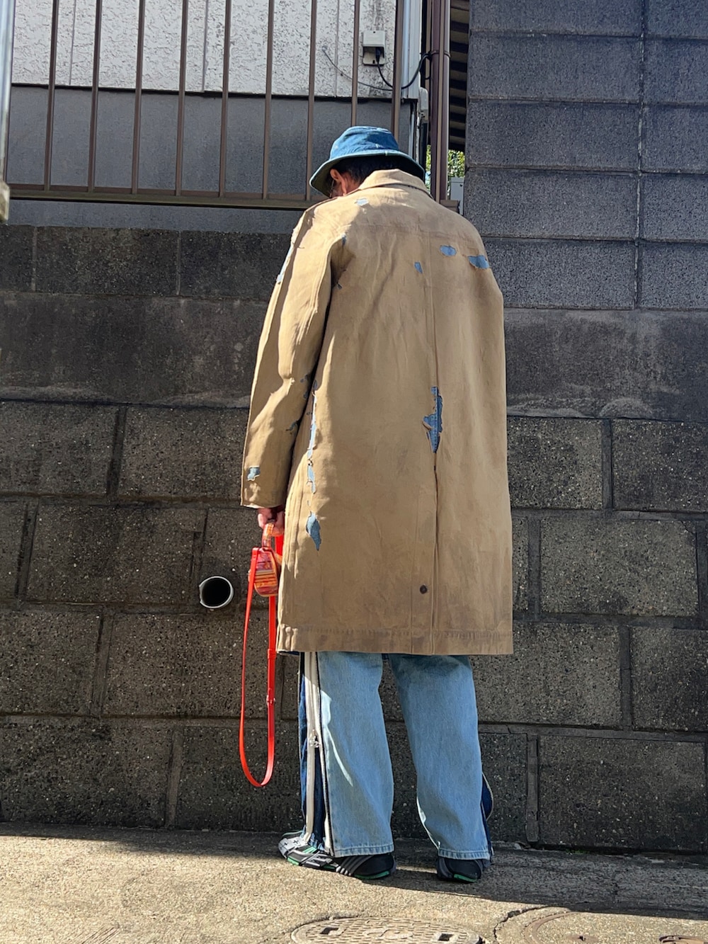 ベージュ系のステンカラーコート、ブルー系のデニムパンツ、ブラック系のスニーカーを着用したメンズの秋コーディネートの2枚目の写真