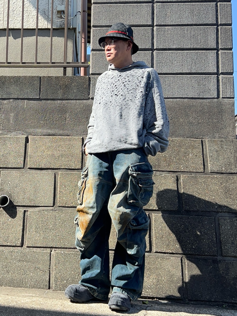 グレー系のパーカー、ブラック系のチェスターコート、ブラック系のブーツを着用したメンズの春コーディネートの4枚目の写真