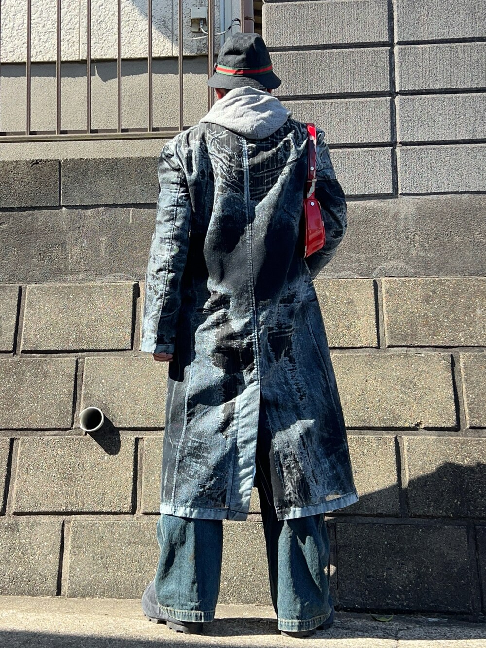 グレー系のパーカー、ブラック系のチェスターコート、ブラック系のブーツを着用したメンズの春コーディネートの3枚目の写真