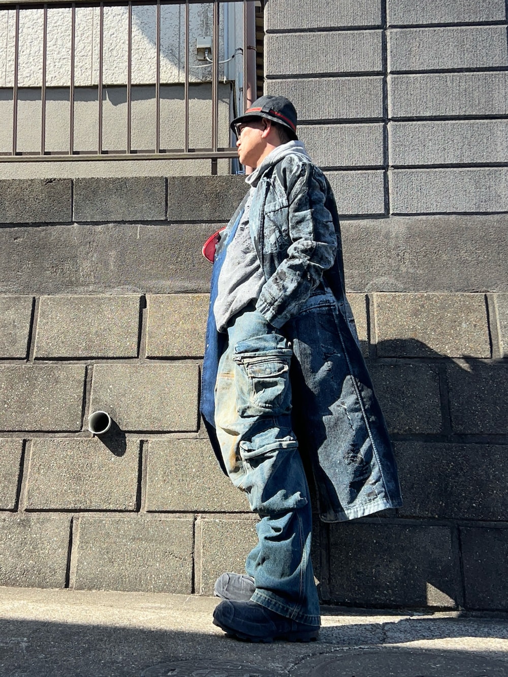 グレー系のパーカー、ブラック系のチェスターコート、ブラック系のブーツを着用したメンズの春コーディネートの2枚目の写真