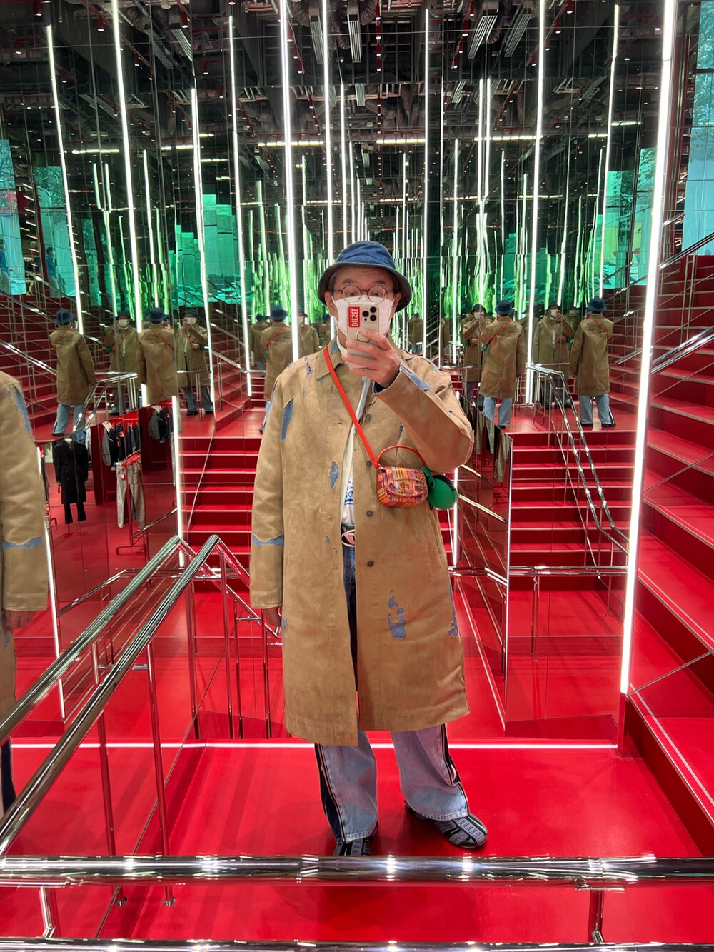 ベージュ系のステンカラーコート、ブルー系のデニムパンツ、ブラック系のスニーカーを着用したメンズの秋コーディネートの3枚目の写真