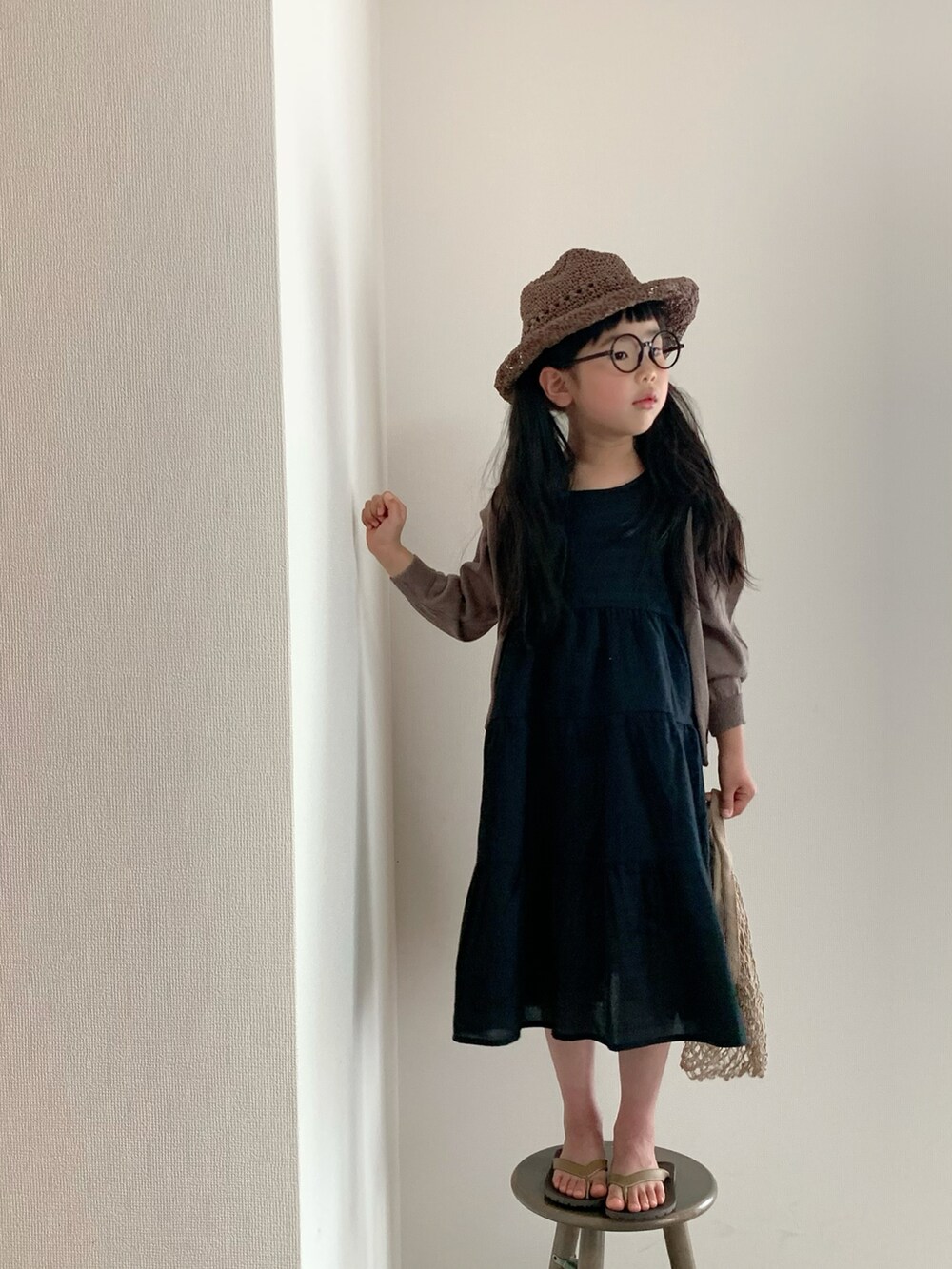 ブラック系のワンピース/ドレス、ブラウン系のサンダル、ブラウン系のハットを着用したキッズの春コーディネートの2枚目の写真