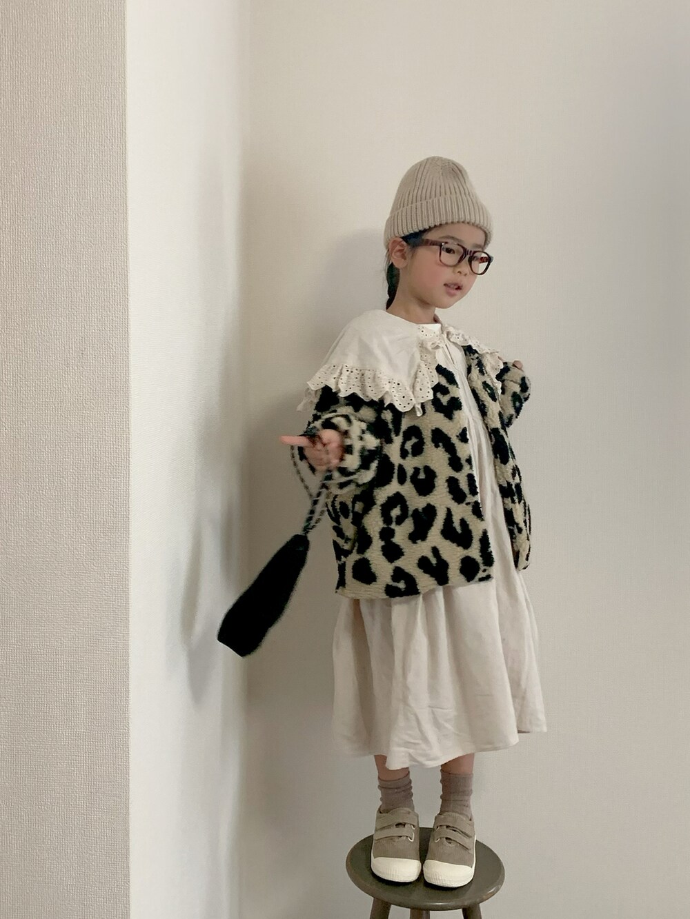 ブラック系のノーカラージャケット、ホワイト系のワンピース、ベージュ系のスニーカーを着用したキッズの秋コーディネートの2枚目の写真