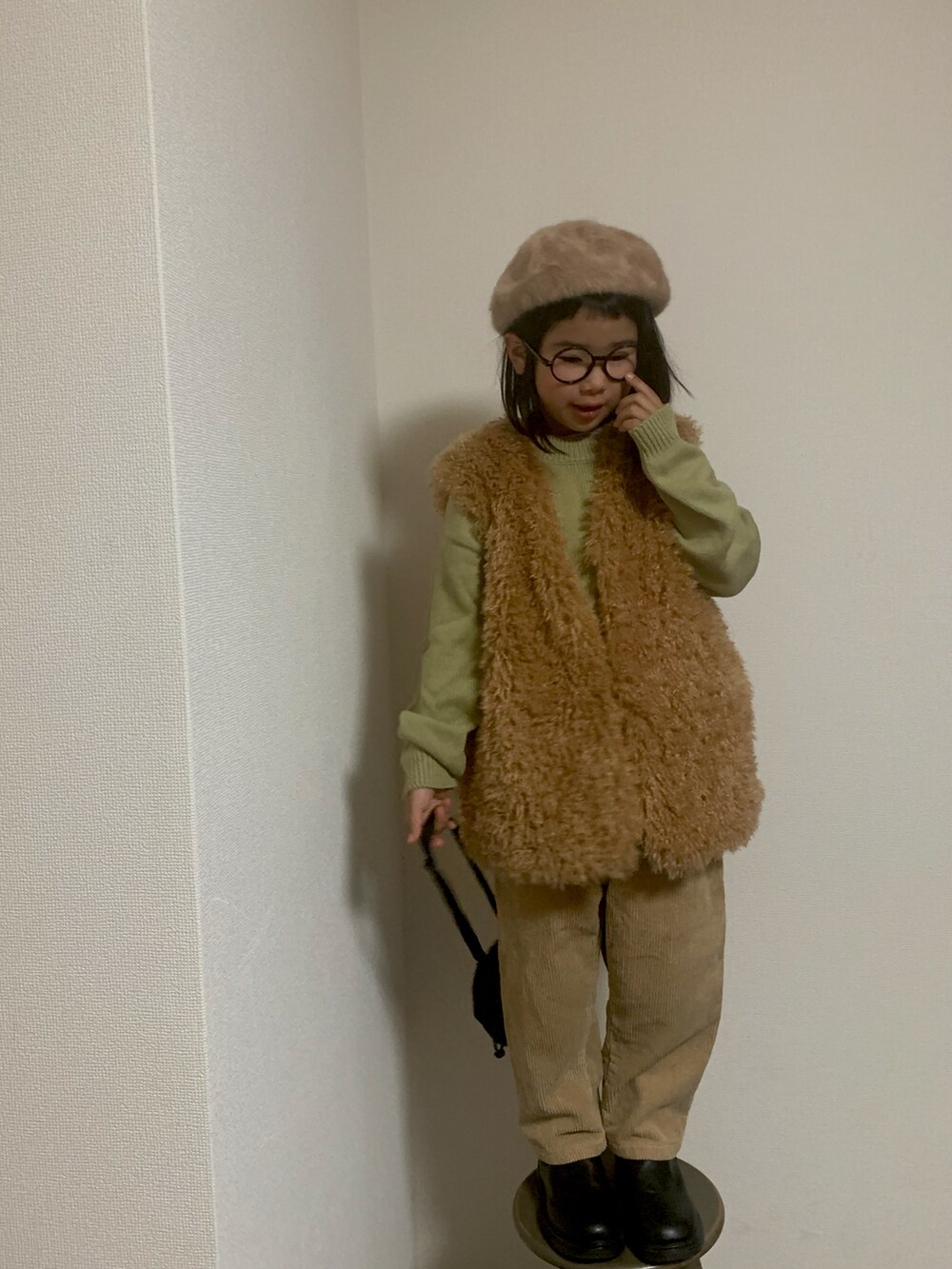 イエロー系のベスト、ベージュ系のパンツ、ブラック系のポーチを着用したキッズの冬コーディネートの3枚目の写真