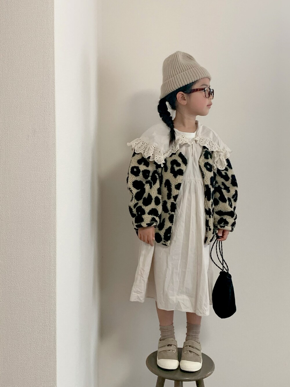 ブラック系のノーカラージャケット、ホワイト系のワンピース、ベージュ系のスニーカーを着用したキッズの秋コーディネートの3枚目の写真