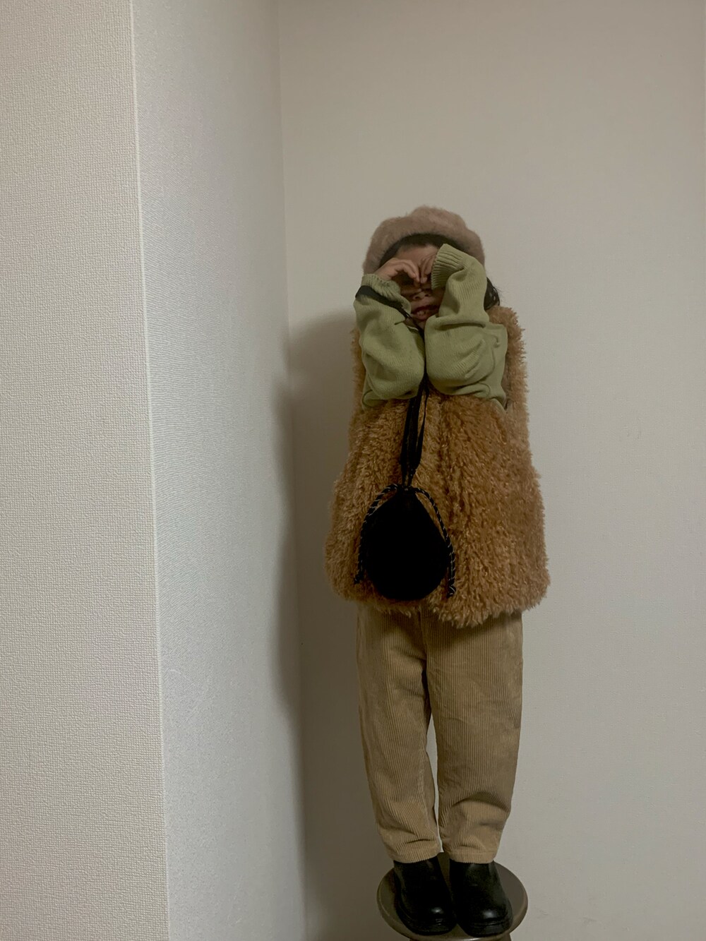 イエロー系のベスト、ベージュ系のパンツ、ブラック系のポーチを着用したキッズの冬コーディネートの2枚目の写真