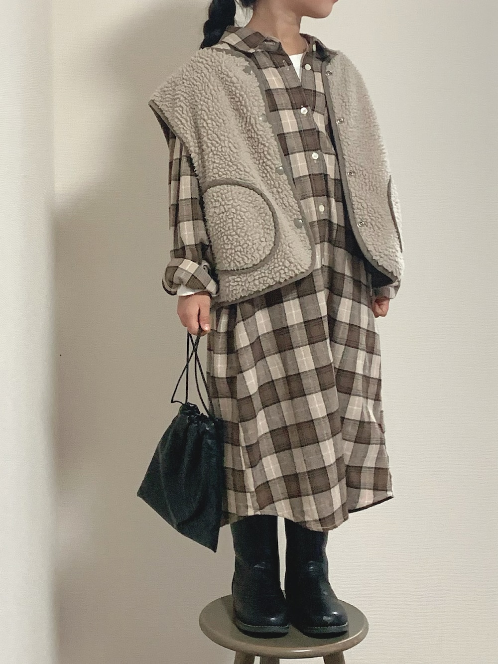 ブラック系のブーツ、ブラウン系のシャツワンピース、ベージュ系のベストを着用したキッズの冬コーディネートの2枚目の写真