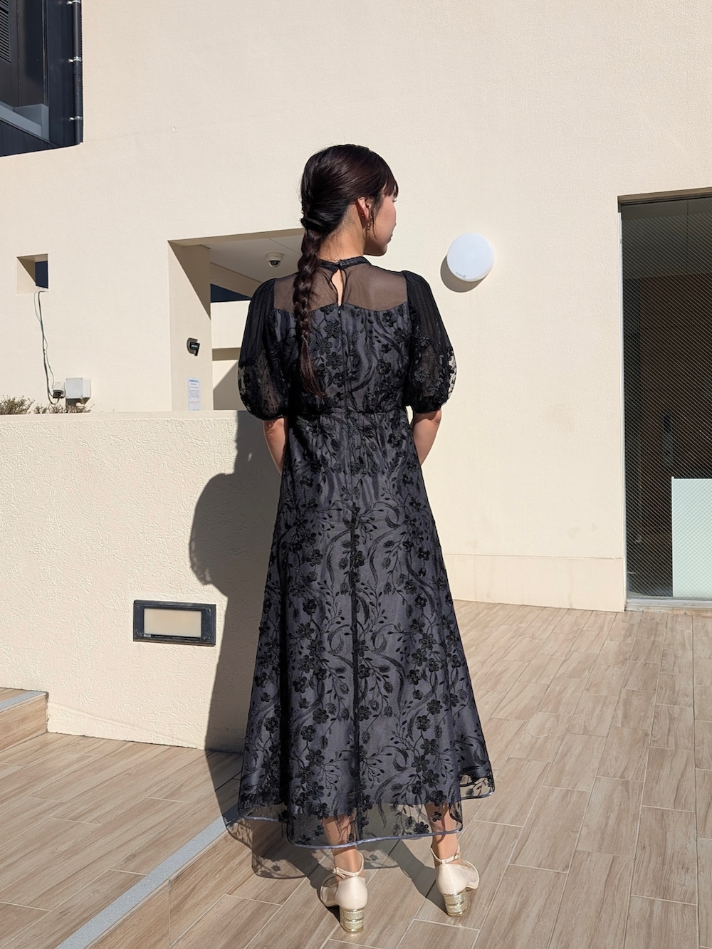 ブラック系のドレス、ベージュ系のクラッチバッグ、ベージュ系のパンプスを着用したレディースの冬コーディネートの2枚目の写真