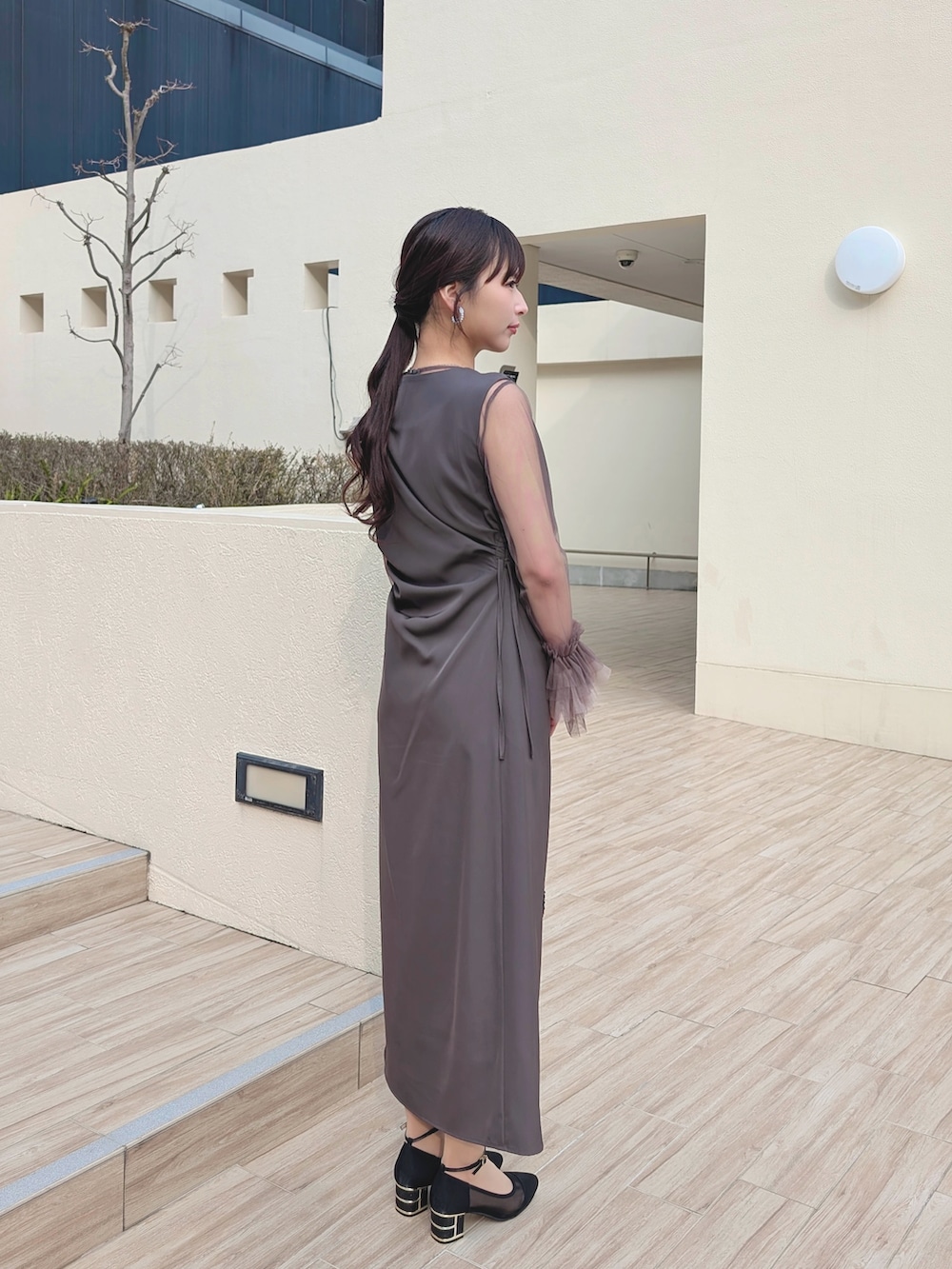 グレー系のドレス、ブラック系のハンドバッグ、ブラック系のパンプスを着用したレディースの冬コーディネートの2枚目の写真