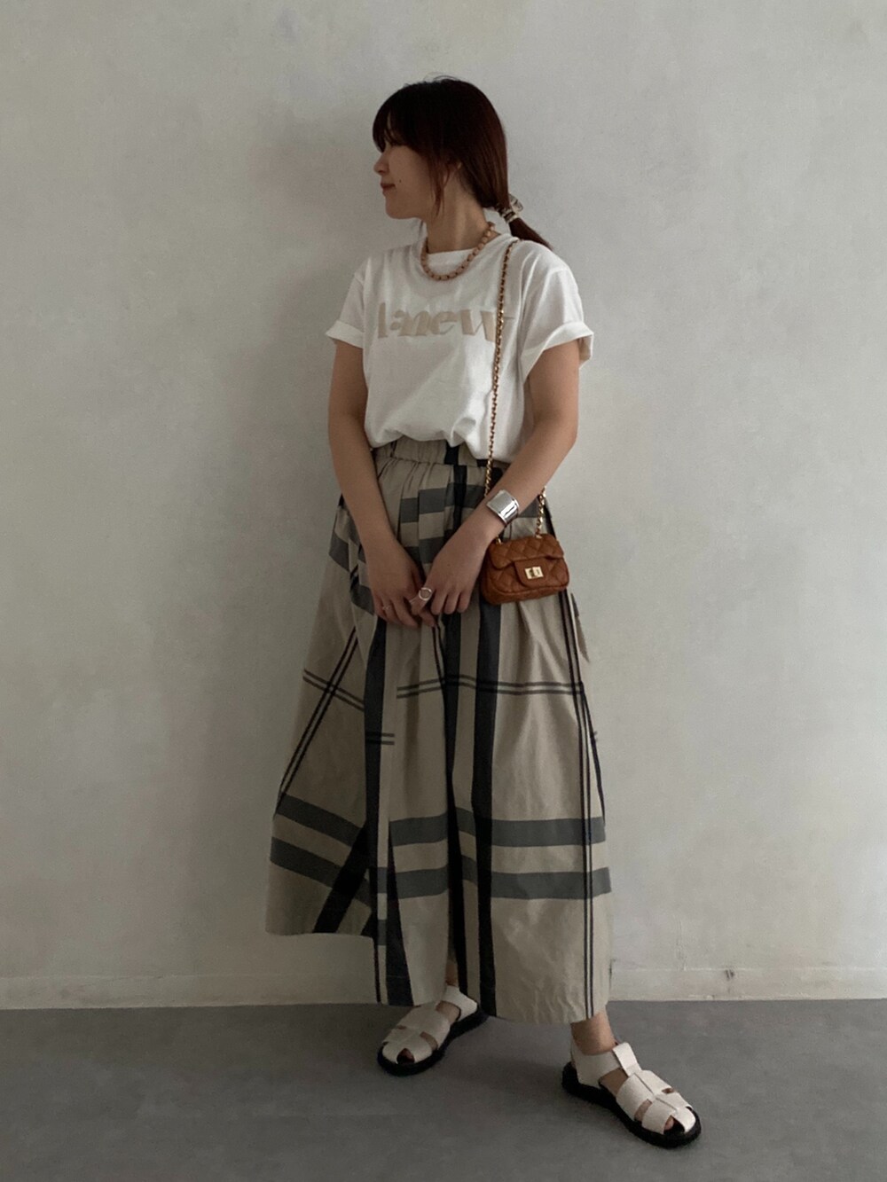 ブラック系のサンダル、ホワイト系のTシャツ/カットソー、ベージュ系のスカートを着用したレディースの夏コーディネートの2枚目の写真