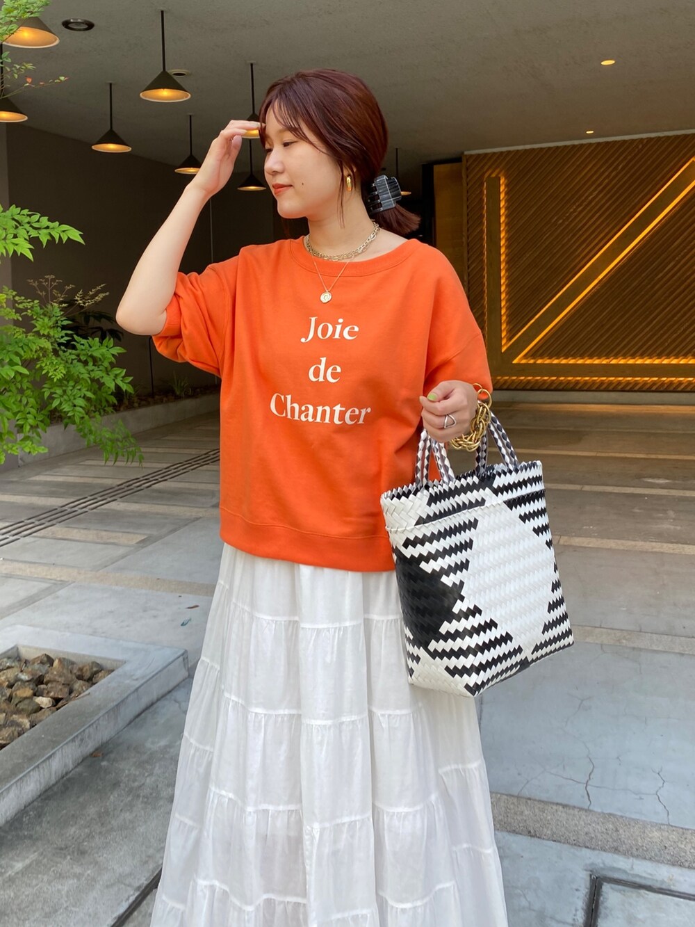 オレンジ系のスウェット、ホワイト系のスカートを着用したレディースの夏コーディネートの4枚目の写真
