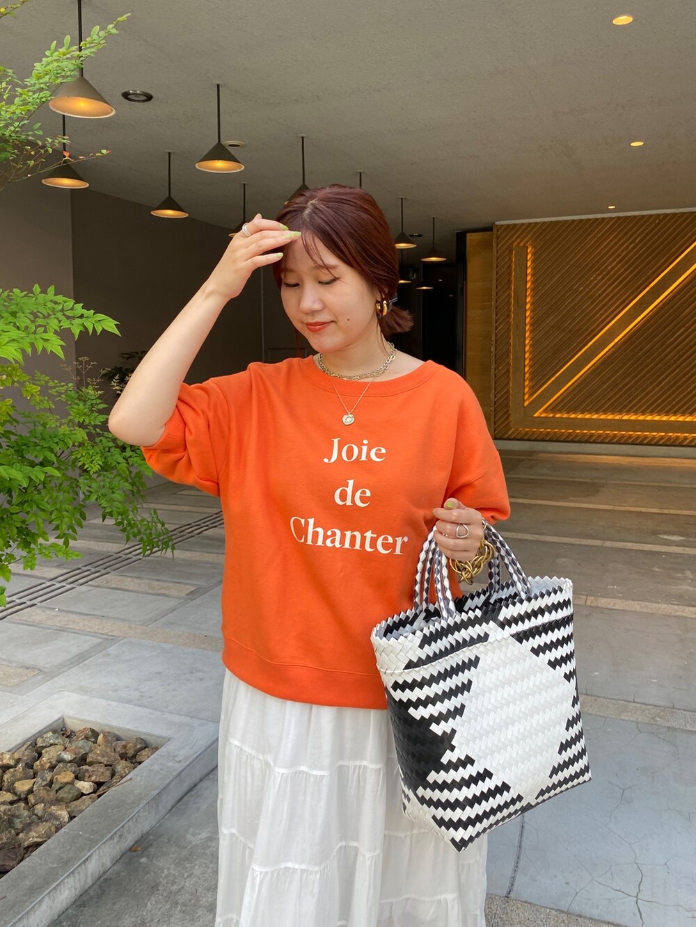 オレンジ系のスウェット、ホワイト系のスカートを着用したレディースの夏コーディネートの7枚目の写真