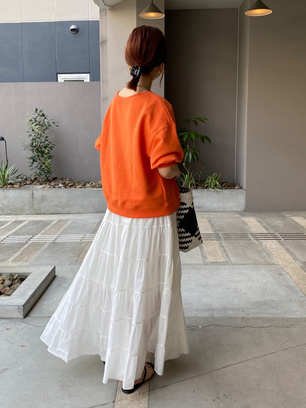 オレンジ系のスウェット、ホワイト系のスカートを着用したレディースの夏コーディネートの5枚目の写真