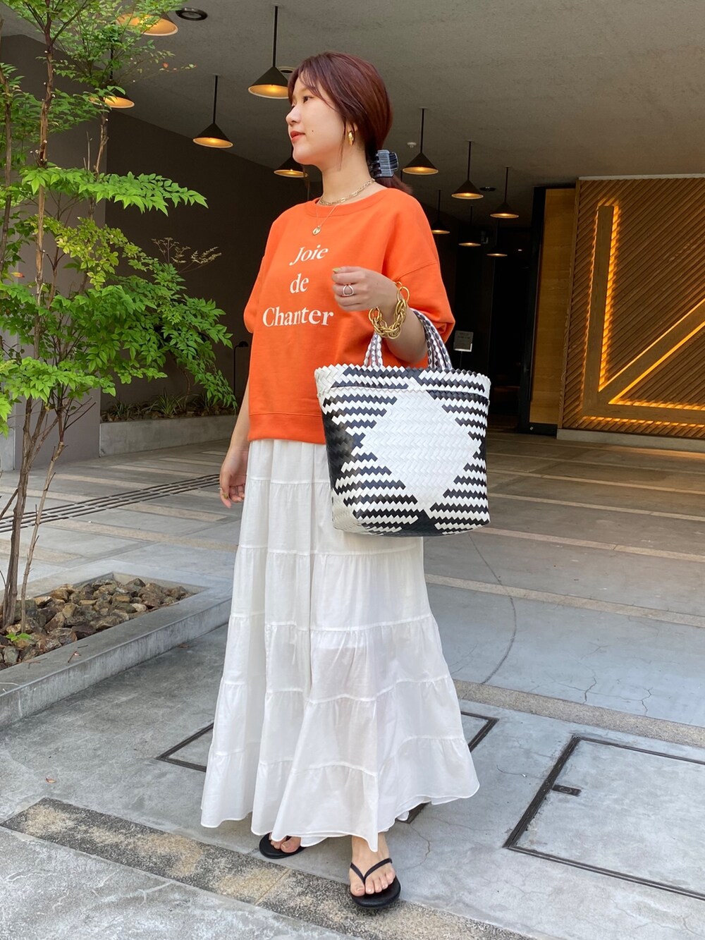 オレンジ系のスウェット、ホワイト系のスカートを着用したレディースの夏コーディネートの2枚目の写真