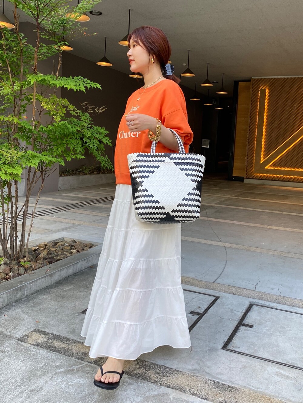 オレンジ系のスウェット、ホワイト系のスカートを着用したレディースの夏コーディネートの3枚目の写真