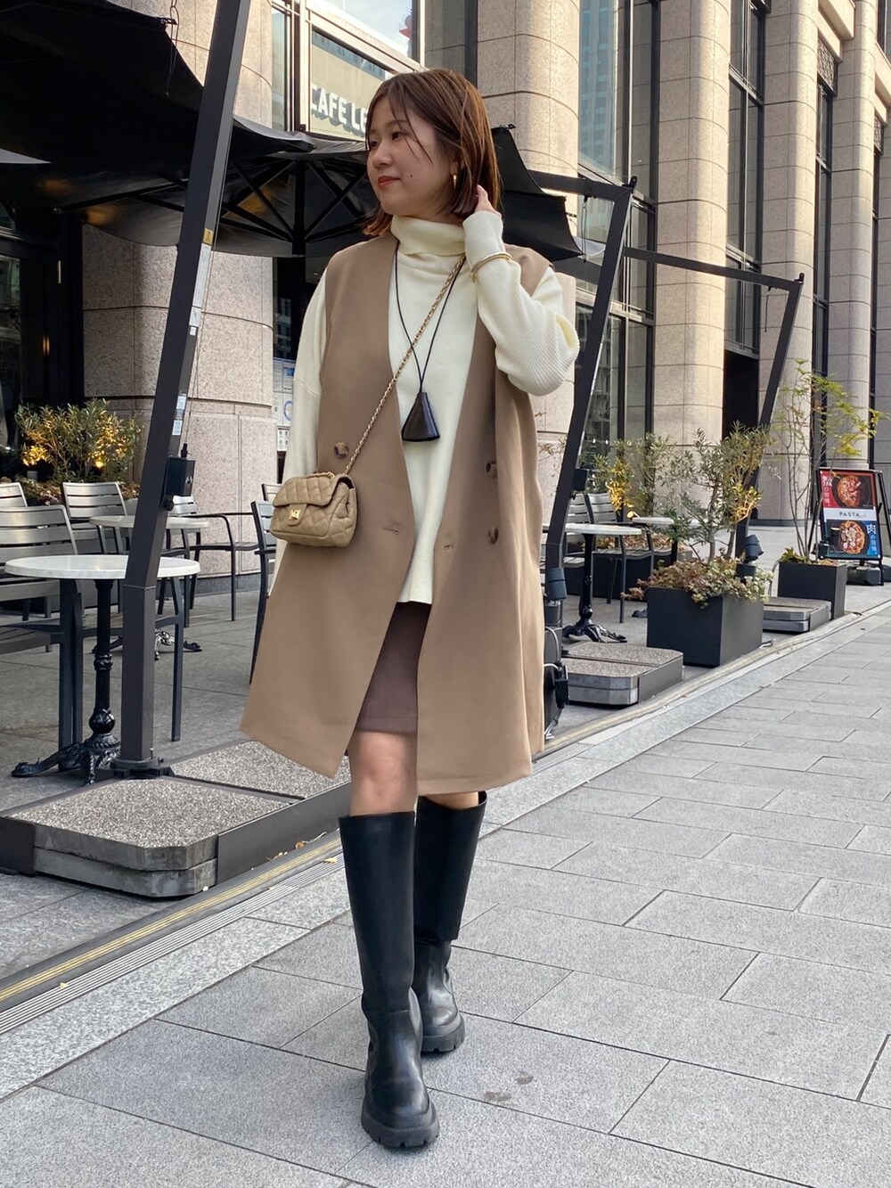 イエロー系のベスト、ホワイト系のニット/セーター、ブラウン系のスカートを着用したレディースの冬コーディネートの2枚目の写真