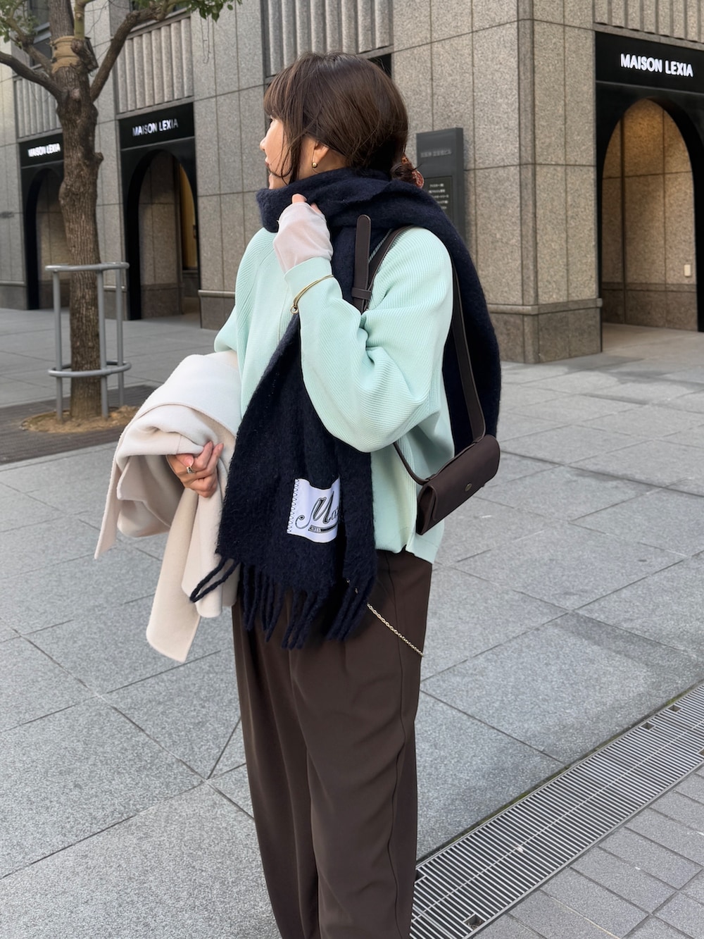 グリーン系のニット/セーター、ブラウン系のスラックス、グレー系のTシャツ/カットソーを着用したレディースの冬コーディネートの2枚目の写真