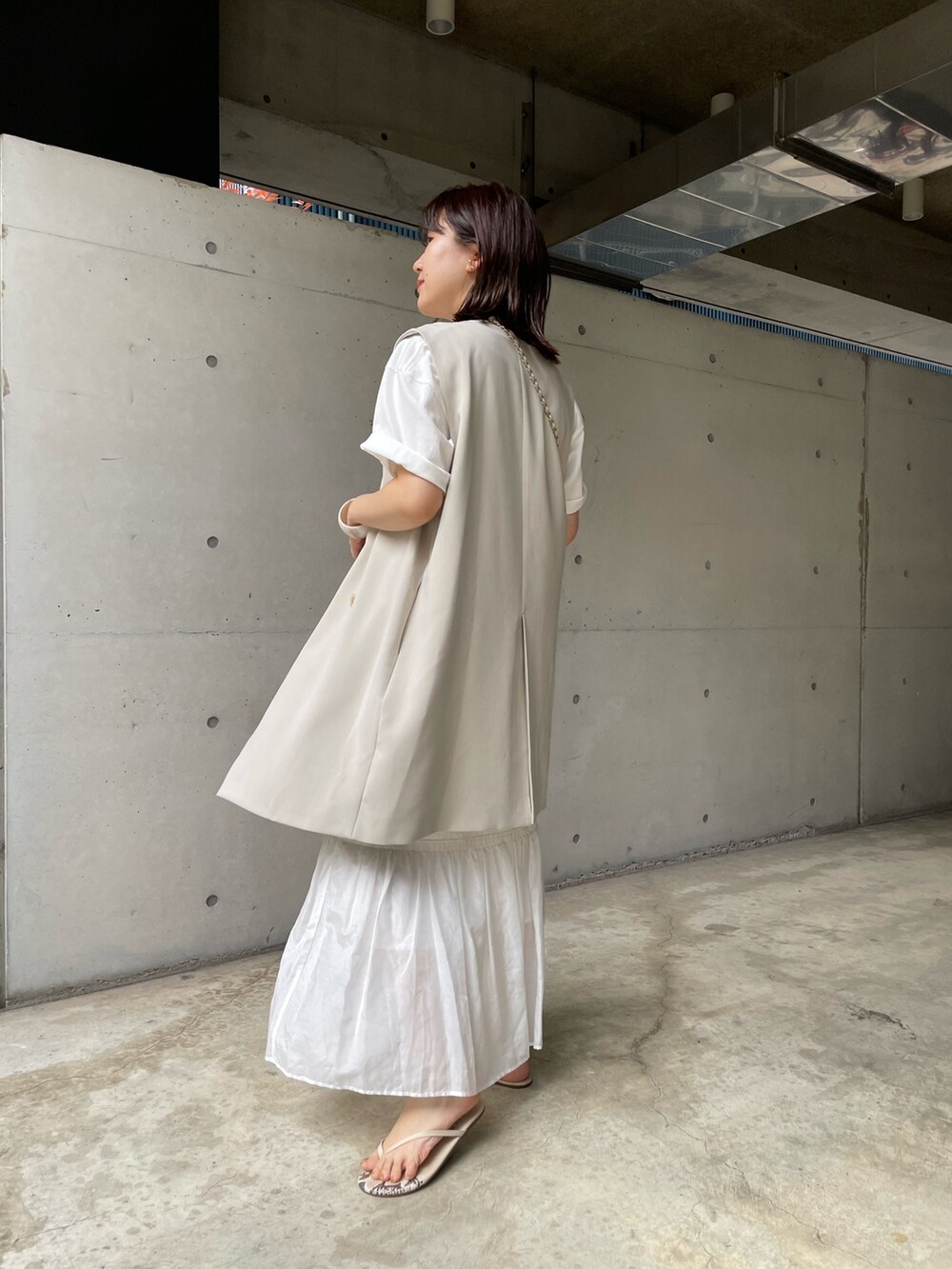 ホワイト系のスカート、ベージュ系のベスト、ホワイト系のショルダーバッグを着用したレディースの夏コーディネートの3枚目の写真