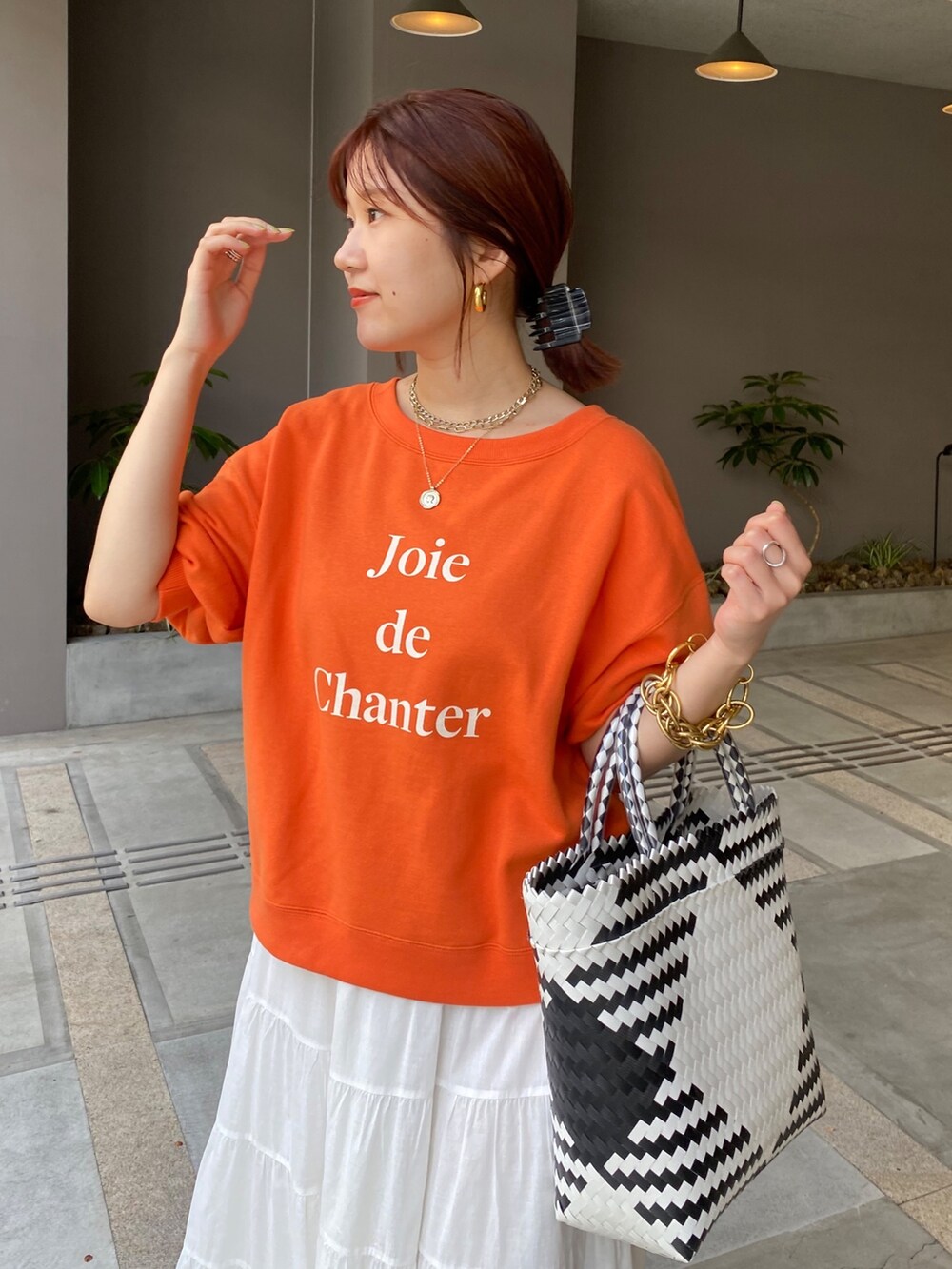 オレンジ系のスウェット、ホワイト系のスカートを着用したレディースの夏コーディネートの6枚目の写真