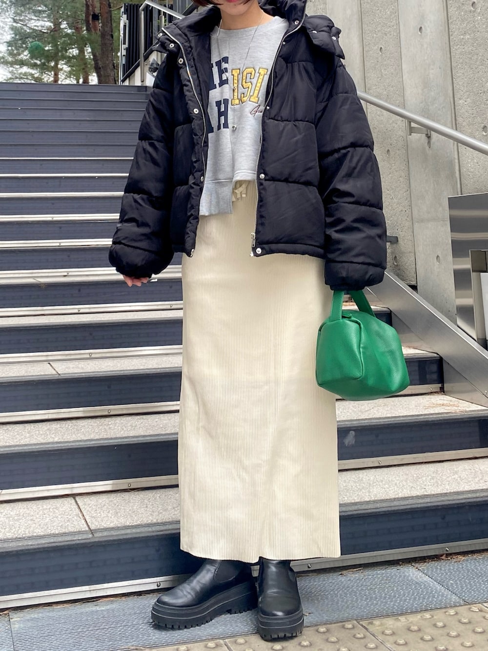 グリーン系のショルダーバッグ、ホワイト系のスカート、ブラック系のブーツを着用したレディースの冬コーディネートの2枚目の写真
