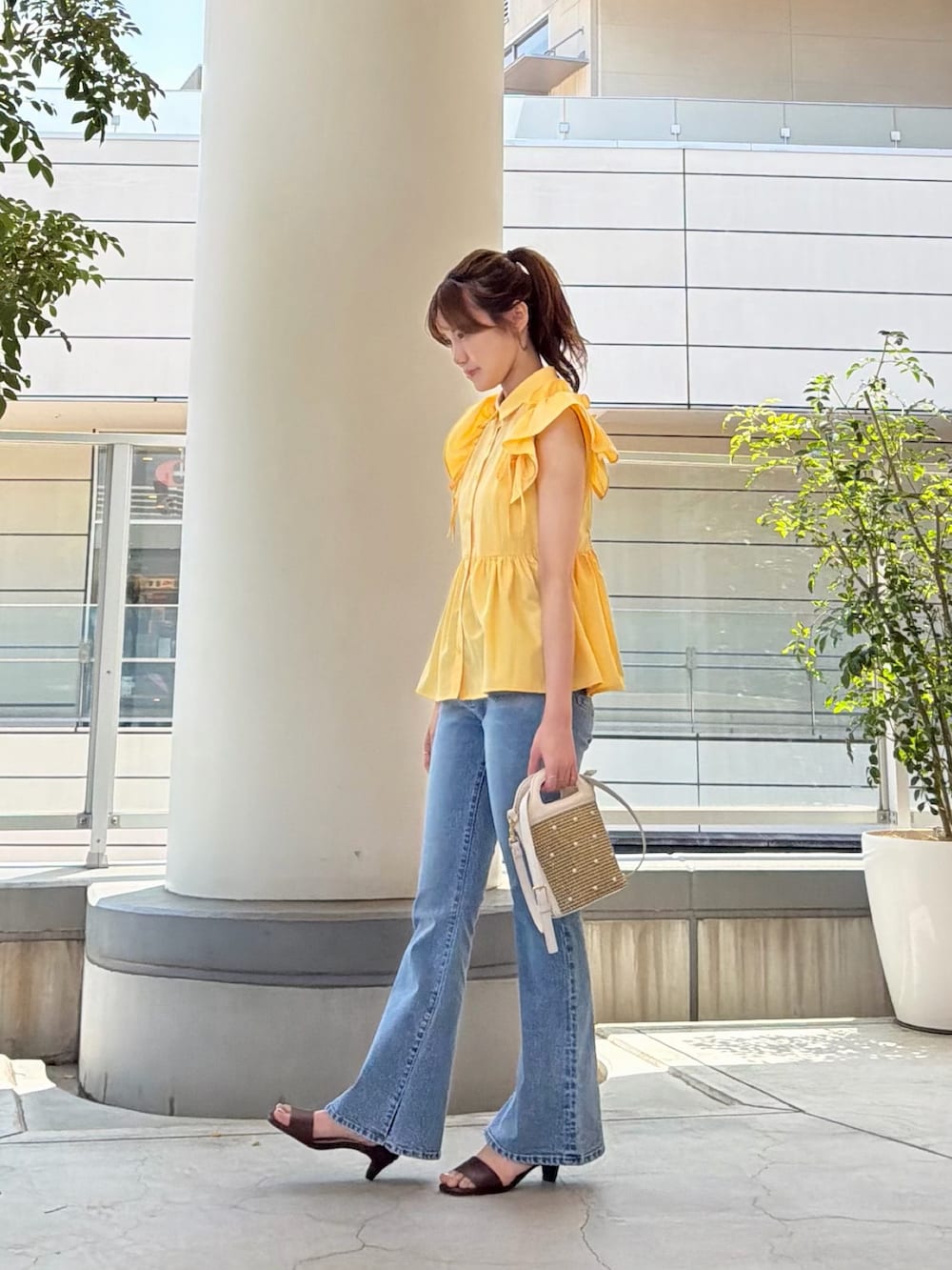 イエロー系のシャツ/ブラウス、ホワイト系のショルダーバッグ、ブルー系のデニムパンツを着用したレディースの夏コーディネートの4枚目の写真