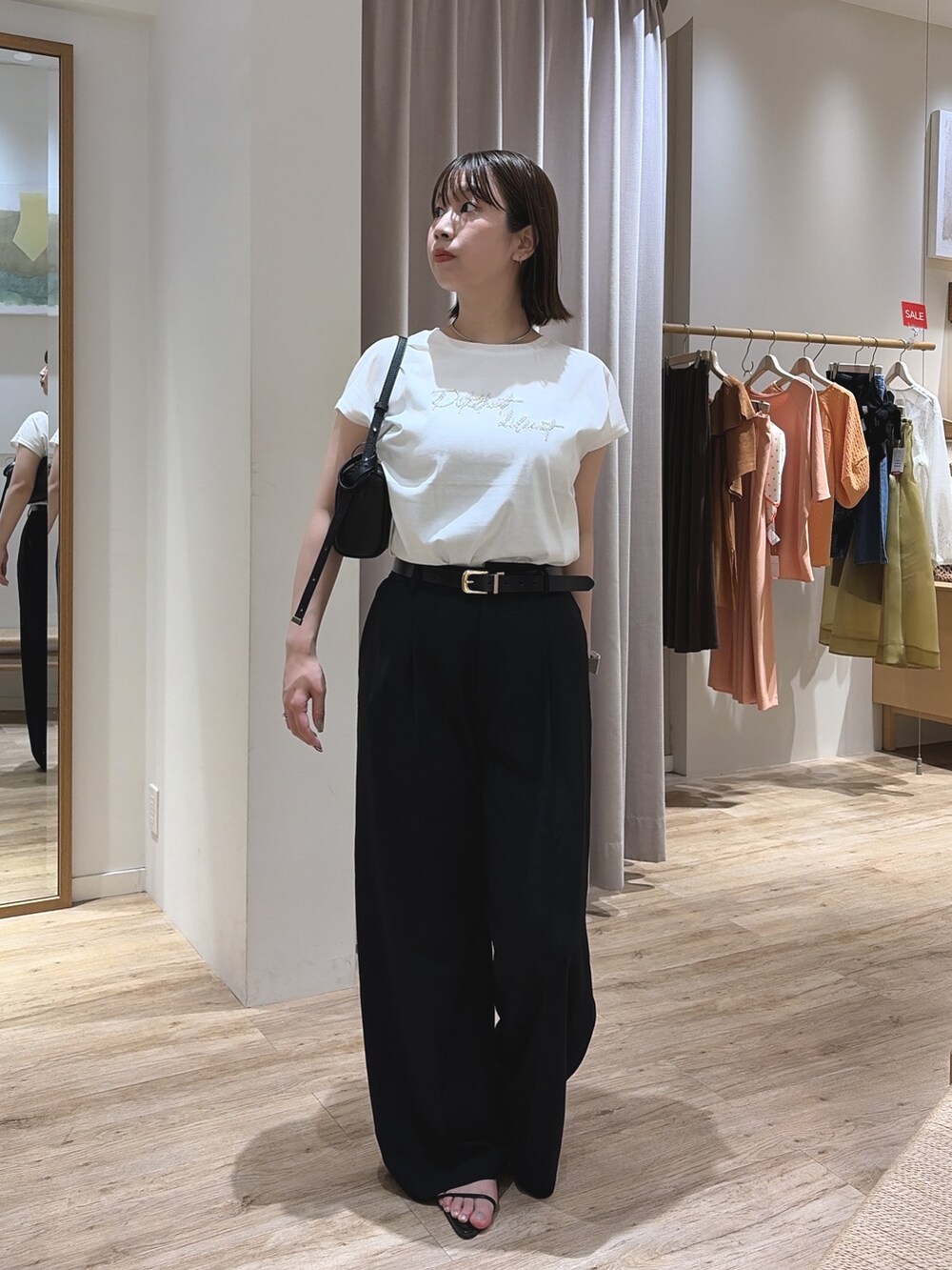ブラック系のスラックス、ブラック系のショルダーバッグ、ホワイト系のTシャツ/カットソーを着用したレディースの夏コーディネートの4枚目の写真