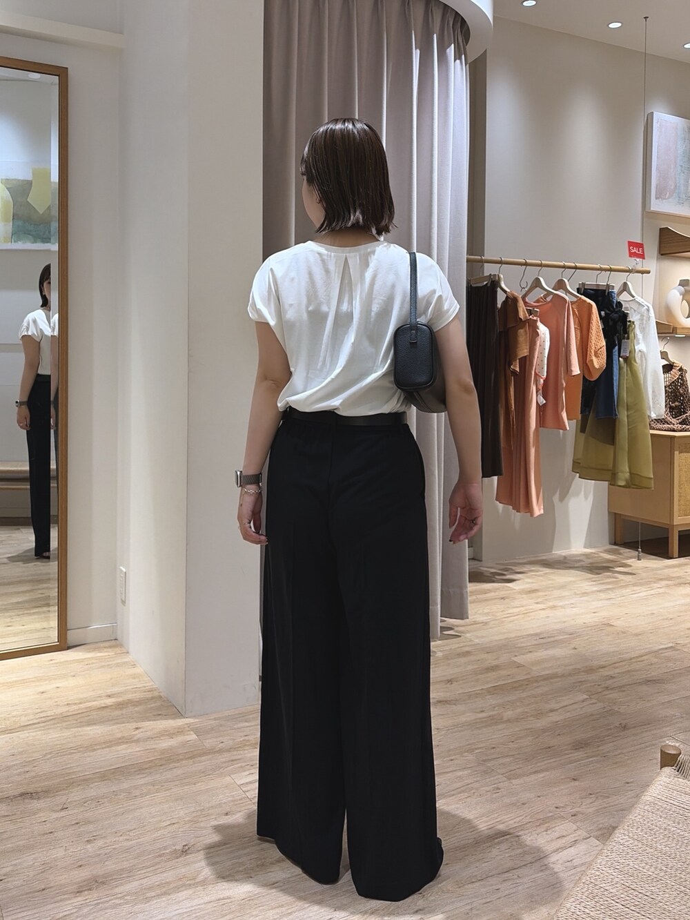 ブラック系のスラックス、ブラック系のショルダーバッグ、ホワイト系のTシャツ/カットソーを着用したレディースの夏コーディネートの3枚目の写真
