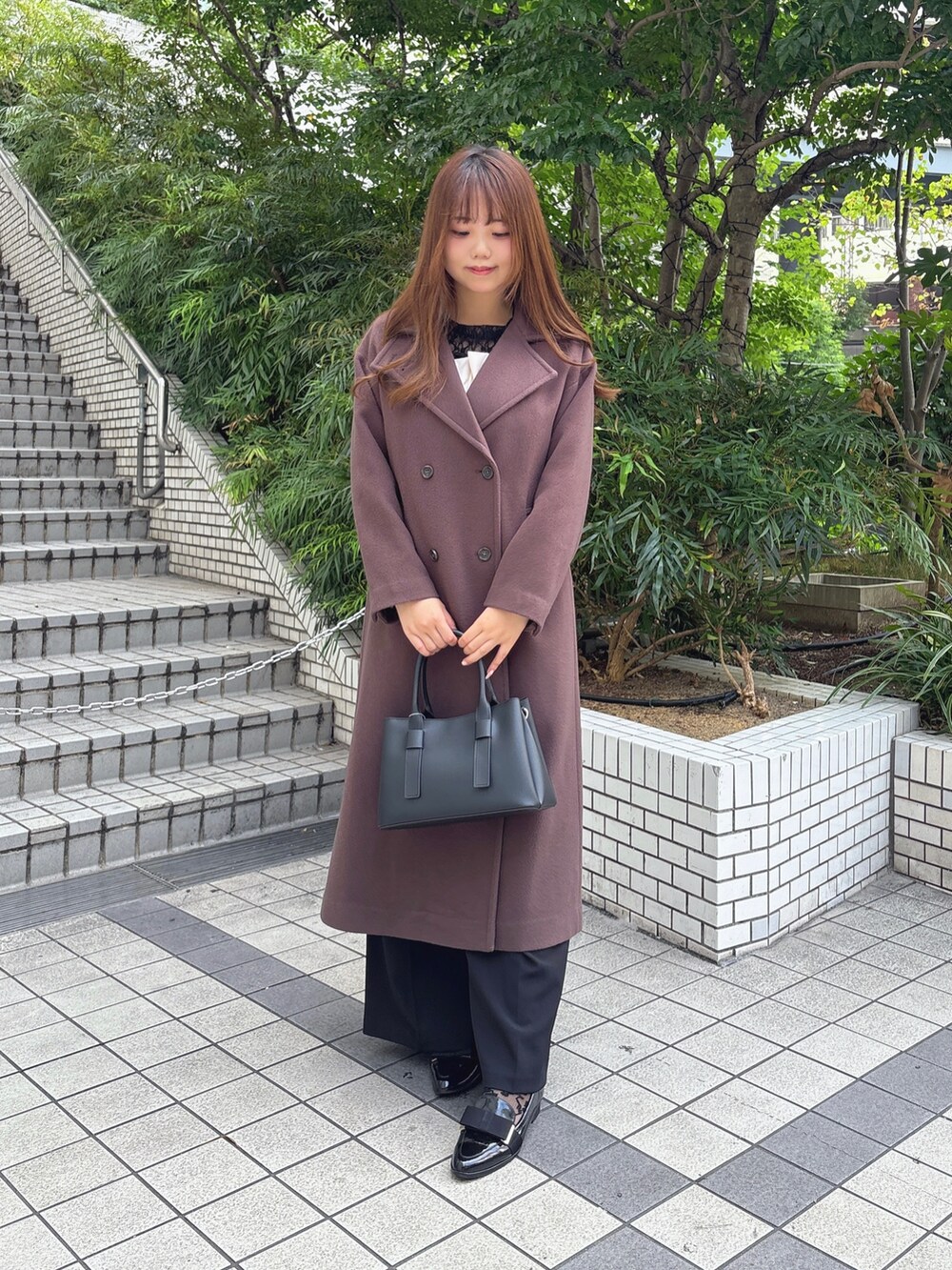 ブラウン系のチェスターコート、ブラック系のつなぎ/オールインワン、ブラック系のTシャツ/カットソーを着用したレディースの秋コーディネートの3枚目の写真