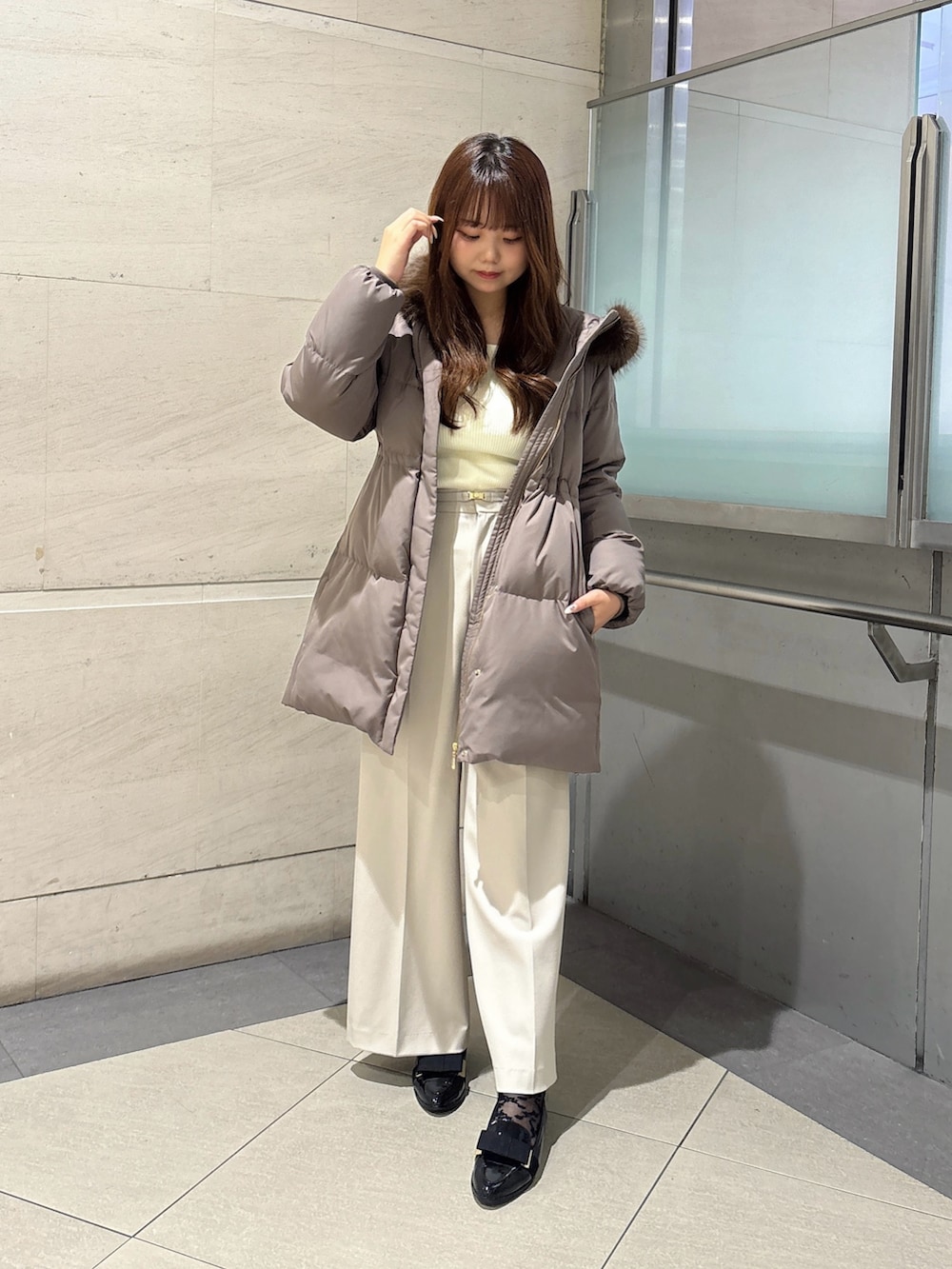 グレー系のその他パンツ、ブラウン系のダウンジャケット/コート、ホワイト系のニット/セーターを着用したレディースの秋コーディネートの2枚目の写真