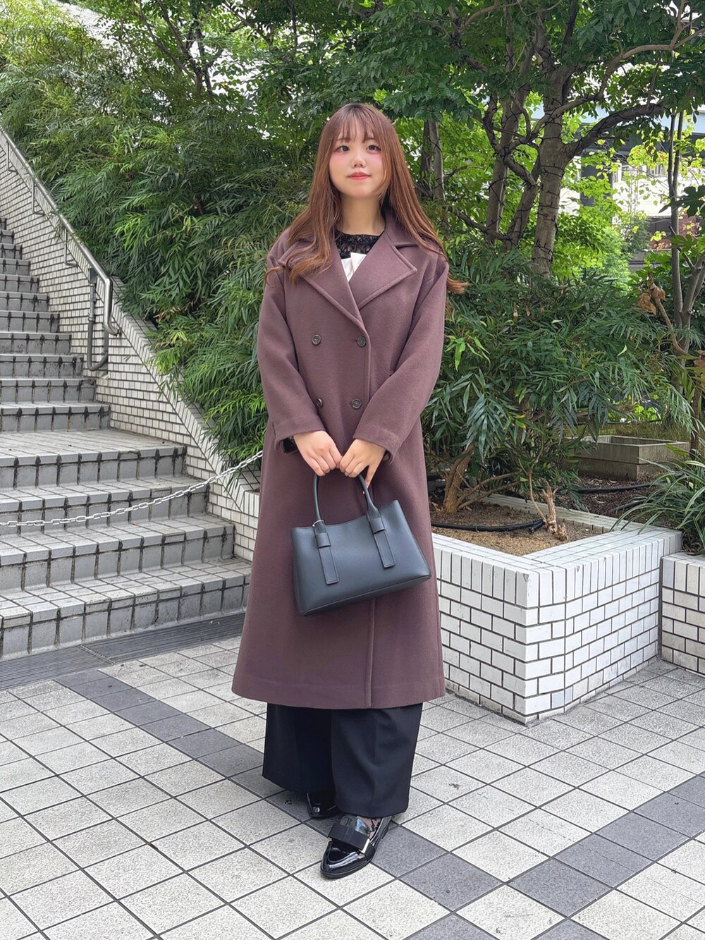 ブラウン系のチェスターコート、ブラック系のつなぎ/オールインワン、ブラック系のTシャツ/カットソーを着用したレディースの秋コーディネートの2枚目の写真
