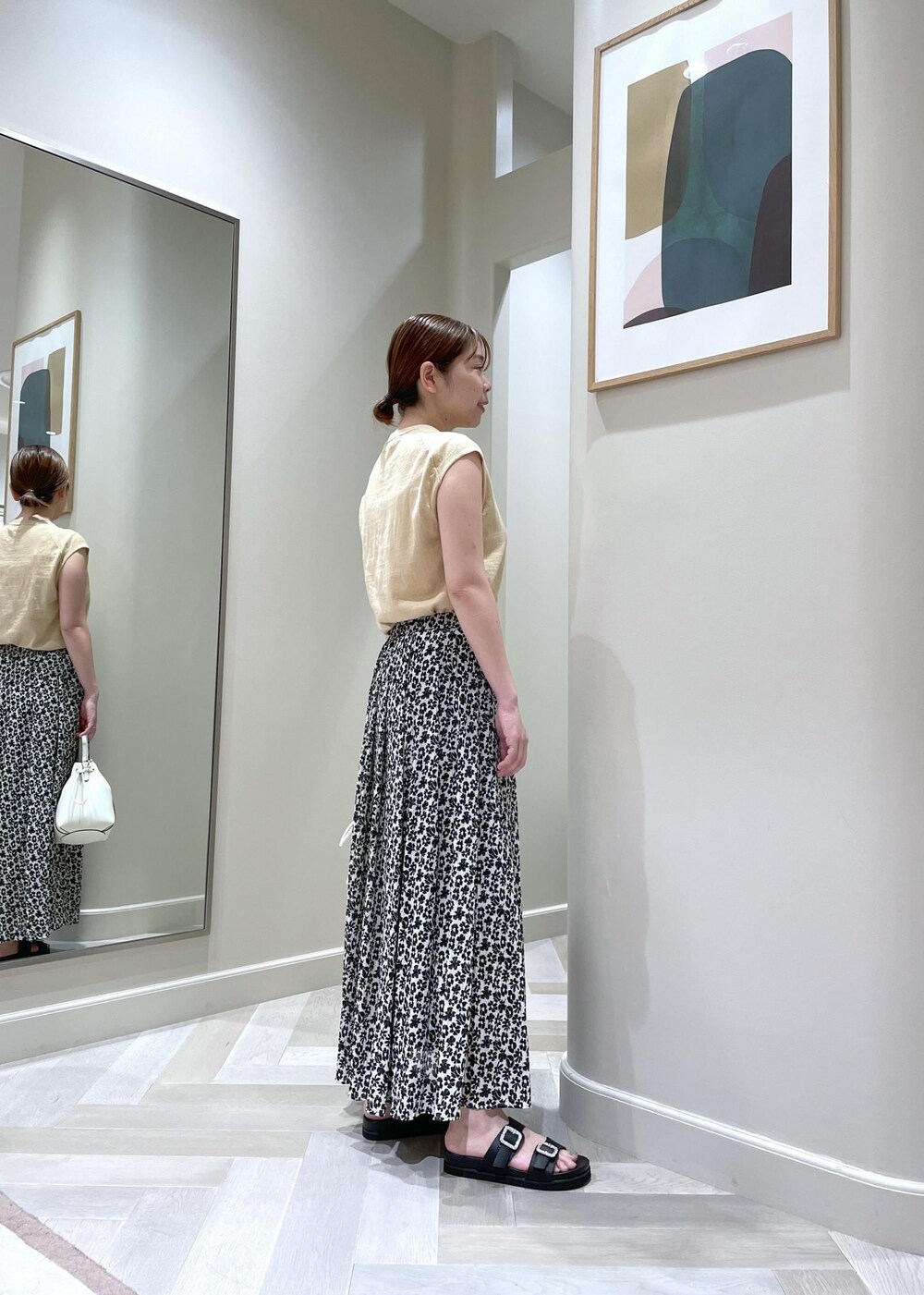 ホワイト系のハンドバッグ、ブラック系のサンダル、ベージュ系のTシャツ/カットソーを着用したレディースの夏コーディネートの2枚目の写真
