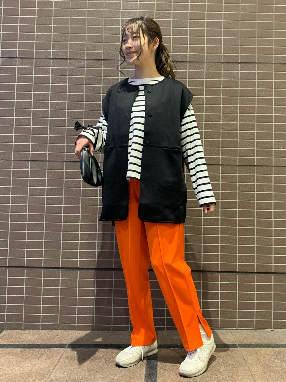 ホワイト系のトップス、ブラック系のベスト、オレンジ系のパンツを着用したレディースの春コーディネートの4枚目の写真