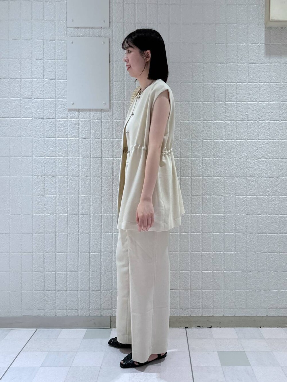 ベージュ系のトートバッグ、ホワイト系のベスト、ホワイト系のキャミソールを着用したレディースの夏コーディネートの2枚目の写真