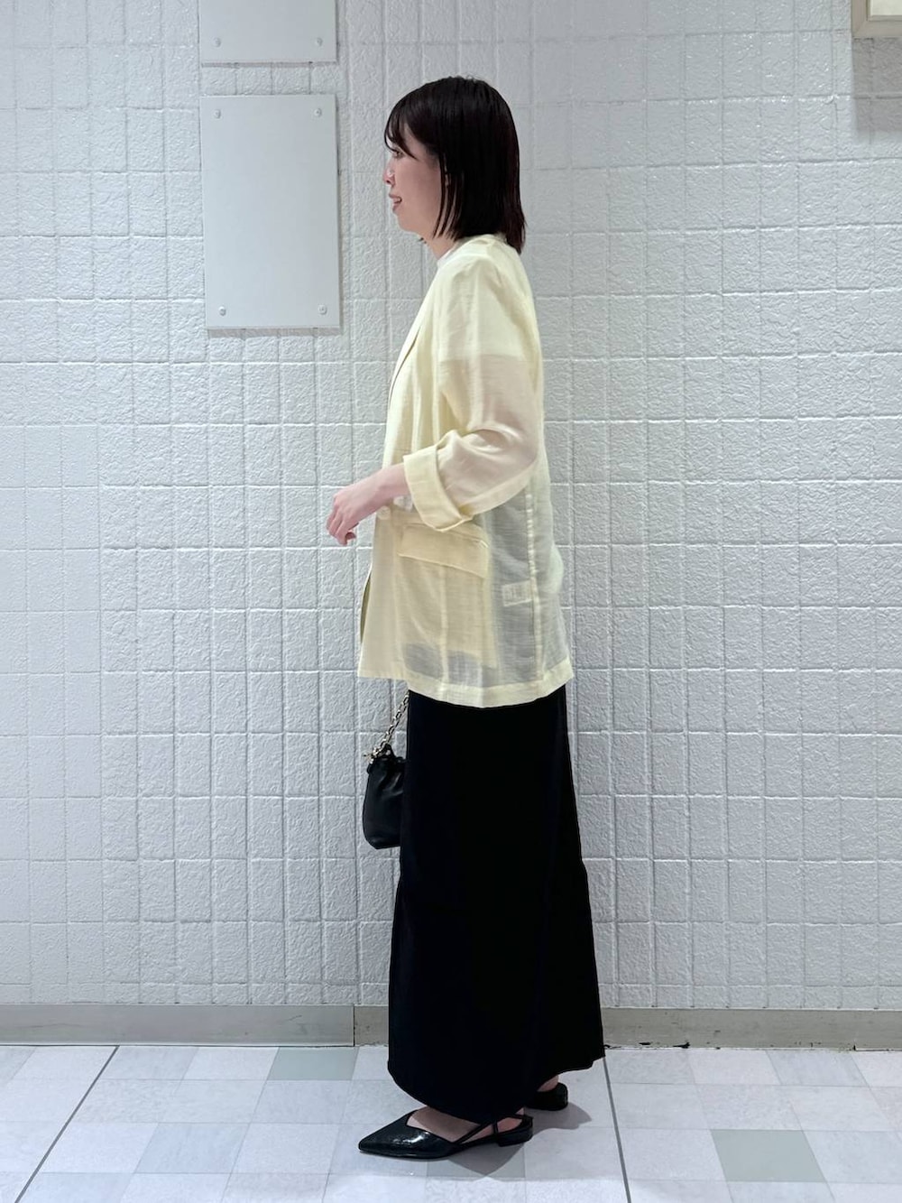 ブラック系のデニムスカート、イエロー系のテーラードジャケット、ブラック系のショルダーバッグを着用したレディースの春コーディネートの2枚目の写真