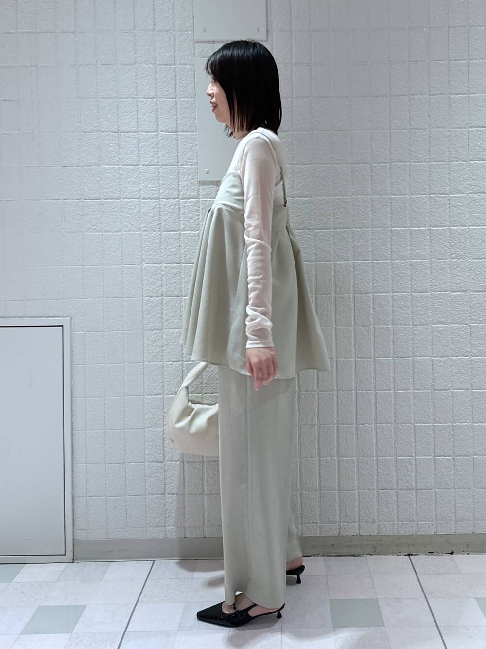 ホワイト系のハンドバッグ、ブラック系のパンプス、ベージュ系のキャミソールを着用したレディースの春コーディネートの2枚目の写真