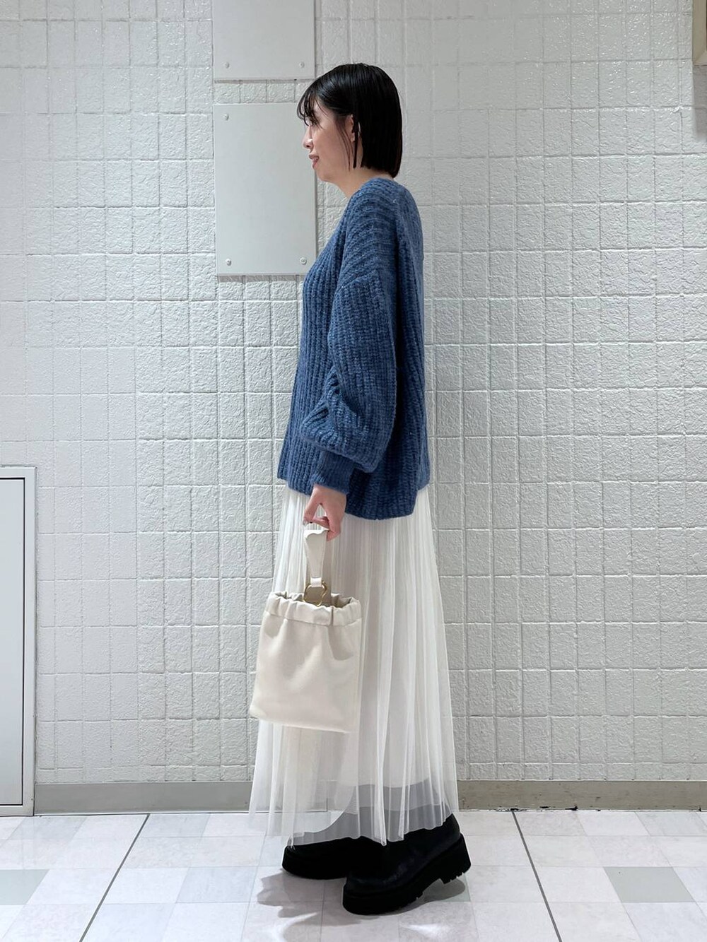 ホワイト系のスカート、ブルー系のニット/セーター、ブラック系のブーツを着用したレディースの冬コーディネートの2枚目の写真