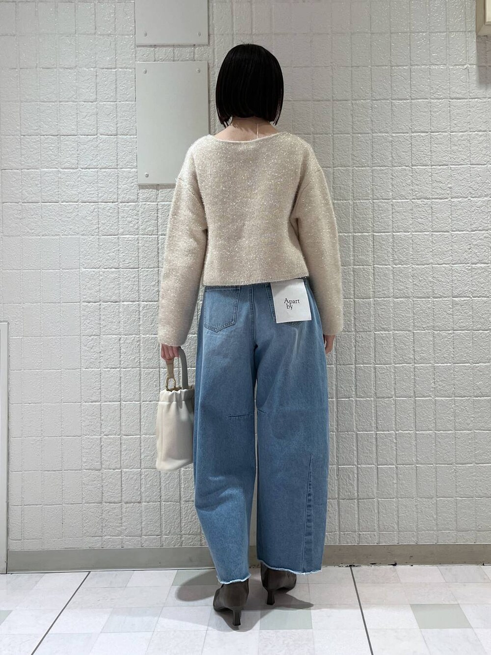 ホワイト系のニット/セーター、ベージュ系のブーツ、ホワイト系のショルダーバッグを着用したレディースの春コーディネートの3枚目の写真