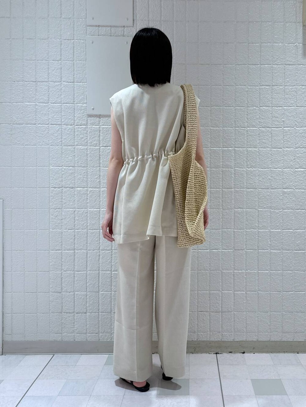 ベージュ系のトートバッグ、ホワイト系のベスト、ホワイト系のキャミソールを着用したレディースの夏コーディネートの3枚目の写真