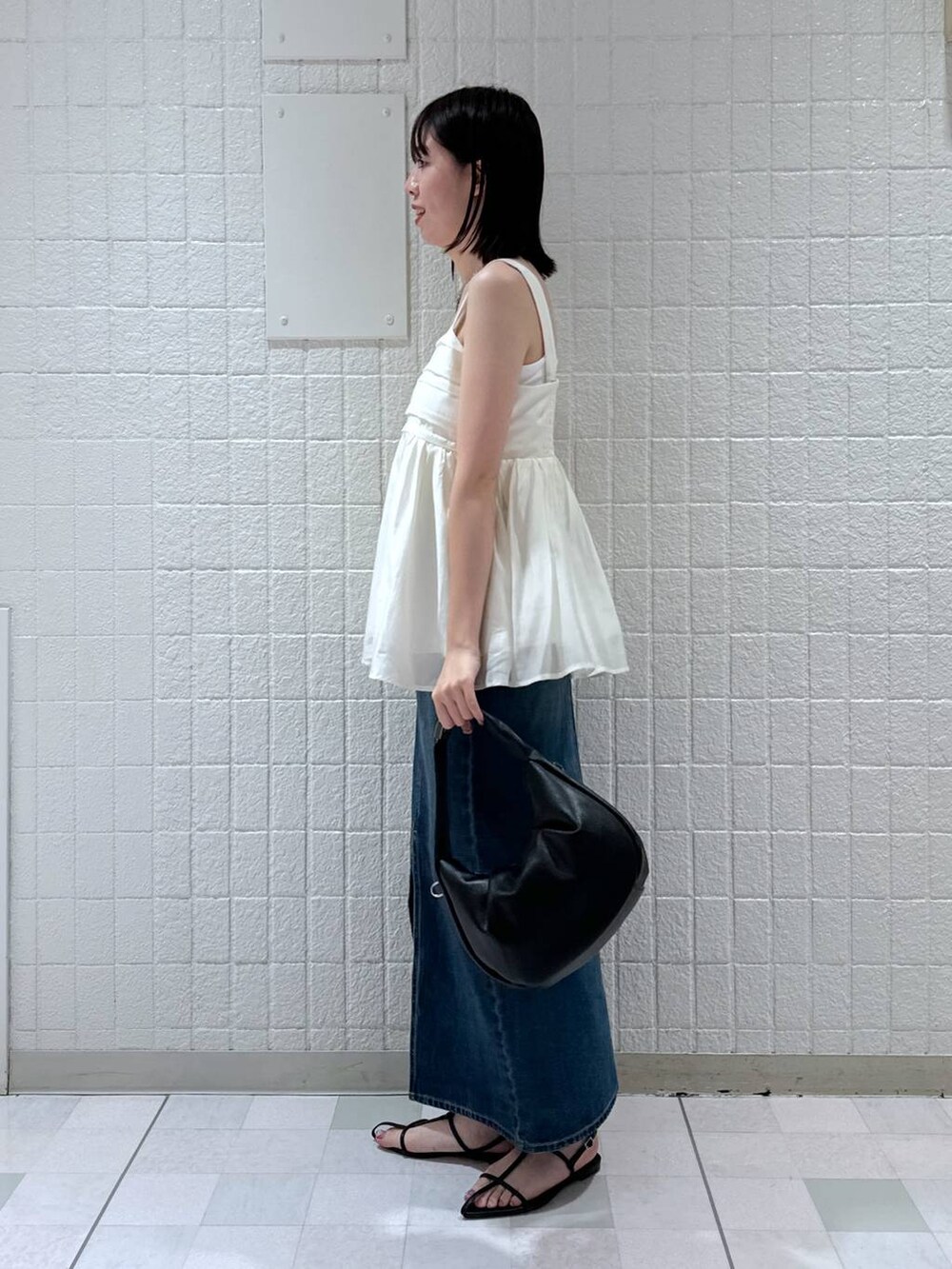 ブラック系のハンドバッグ、ブルー系のデニムスカート、ブラック系のサンダルを着用したレディースの夏コーディネートの2枚目の写真