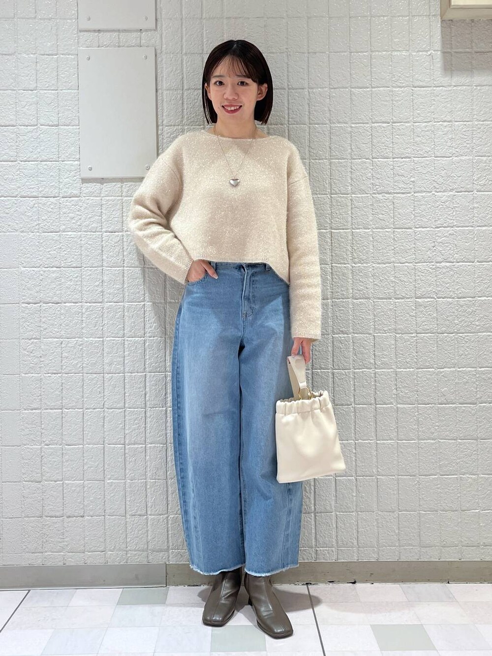 ホワイト系のニット/セーター、ベージュ系のブーツ、ホワイト系のショルダーバッグを着用したレディースの春コーディネートの4枚目の写真