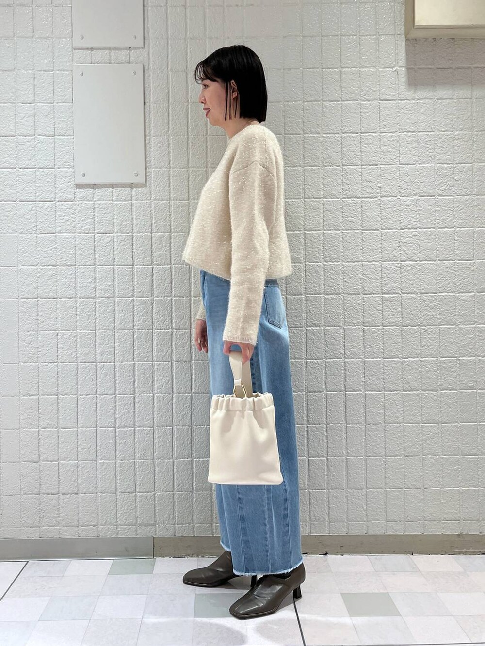 ホワイト系のニット/セーター、ベージュ系のブーツ、ホワイト系のショルダーバッグを着用したレディースの春コーディネートの2枚目の写真
