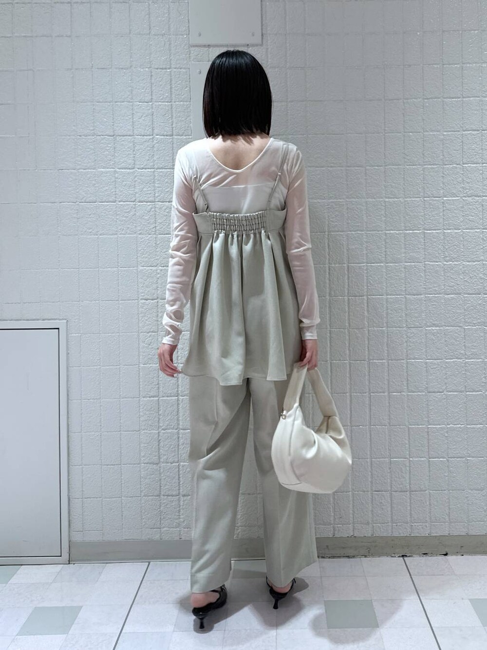 ホワイト系のハンドバッグ、ブラック系のパンプス、ベージュ系のキャミソールを着用したレディースの春コーディネートの3枚目の写真