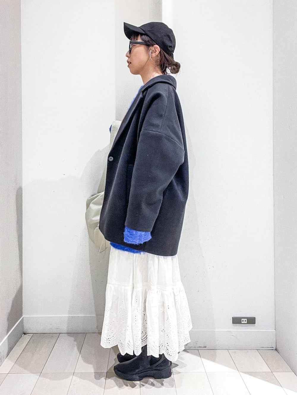 グレー系のステンカラーコート、ホワイト系のショルダーバッグ、ブルー系のニット/セーターを着用したレディースの冬コーディネートの3枚目の写真