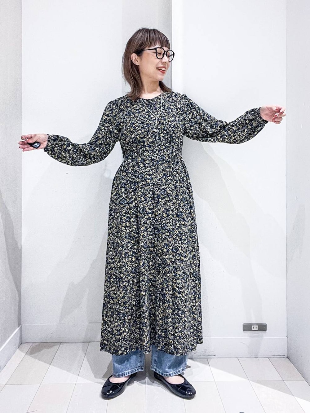 ブルー系のデニムパンツ、ブラック系のワンピース、ブラック系のバレエシューズを着用したレディースの秋コーディネートの6枚目の写真