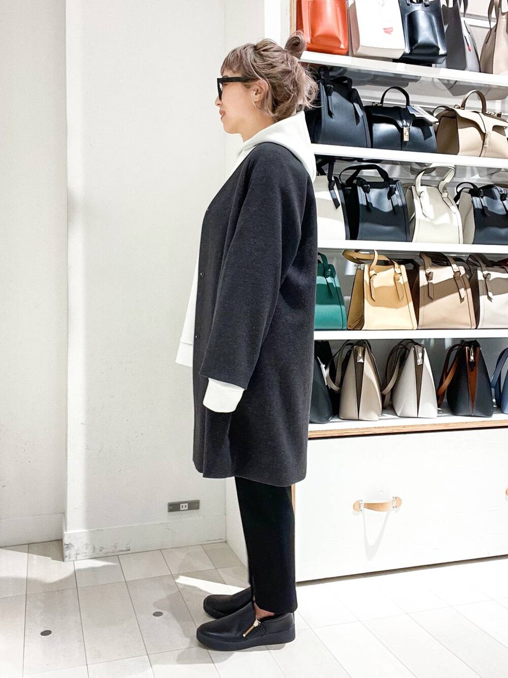 グレー系のノーカラーコート、ホワイト系のパーカー、グリーン系のショルダーバッグを着用したレディースの冬コーディネートの5枚目の写真