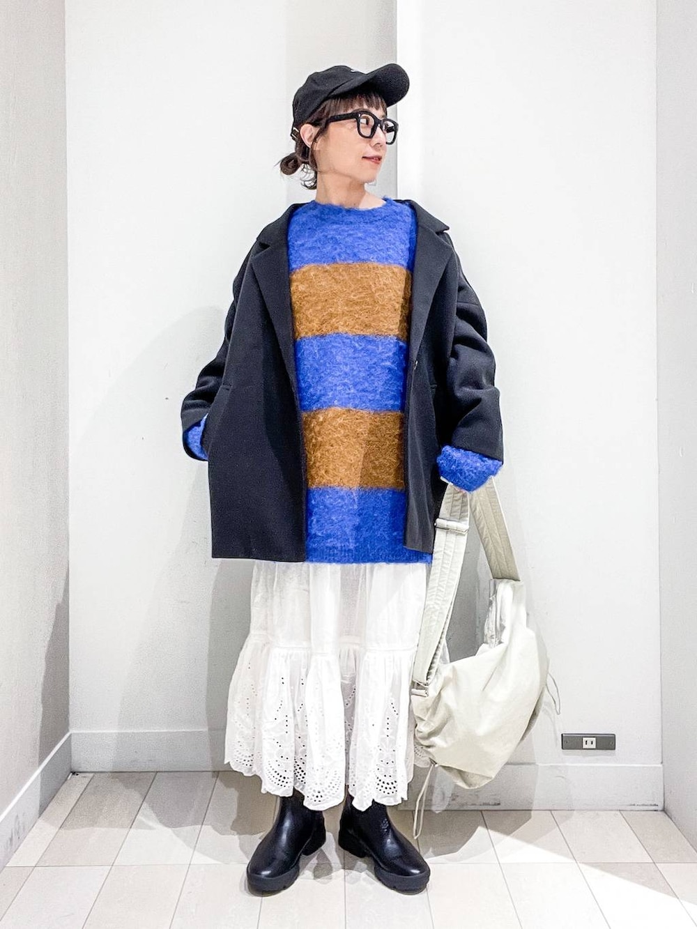 グレー系のステンカラーコート、ホワイト系のショルダーバッグ、ブルー系のニット/セーターを着用したレディースの冬コーディネートの2枚目の写真