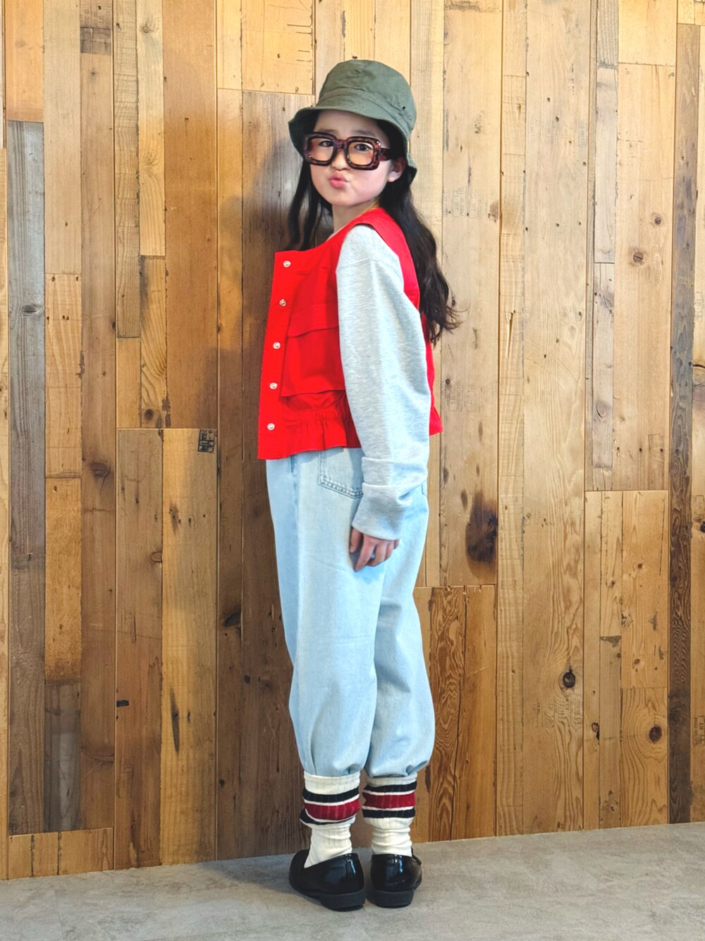 レッド系のベスト、グレー系のスウェット、ブルー系のデニムパンツを着用したキッズの冬コーディネートの2枚目の写真
