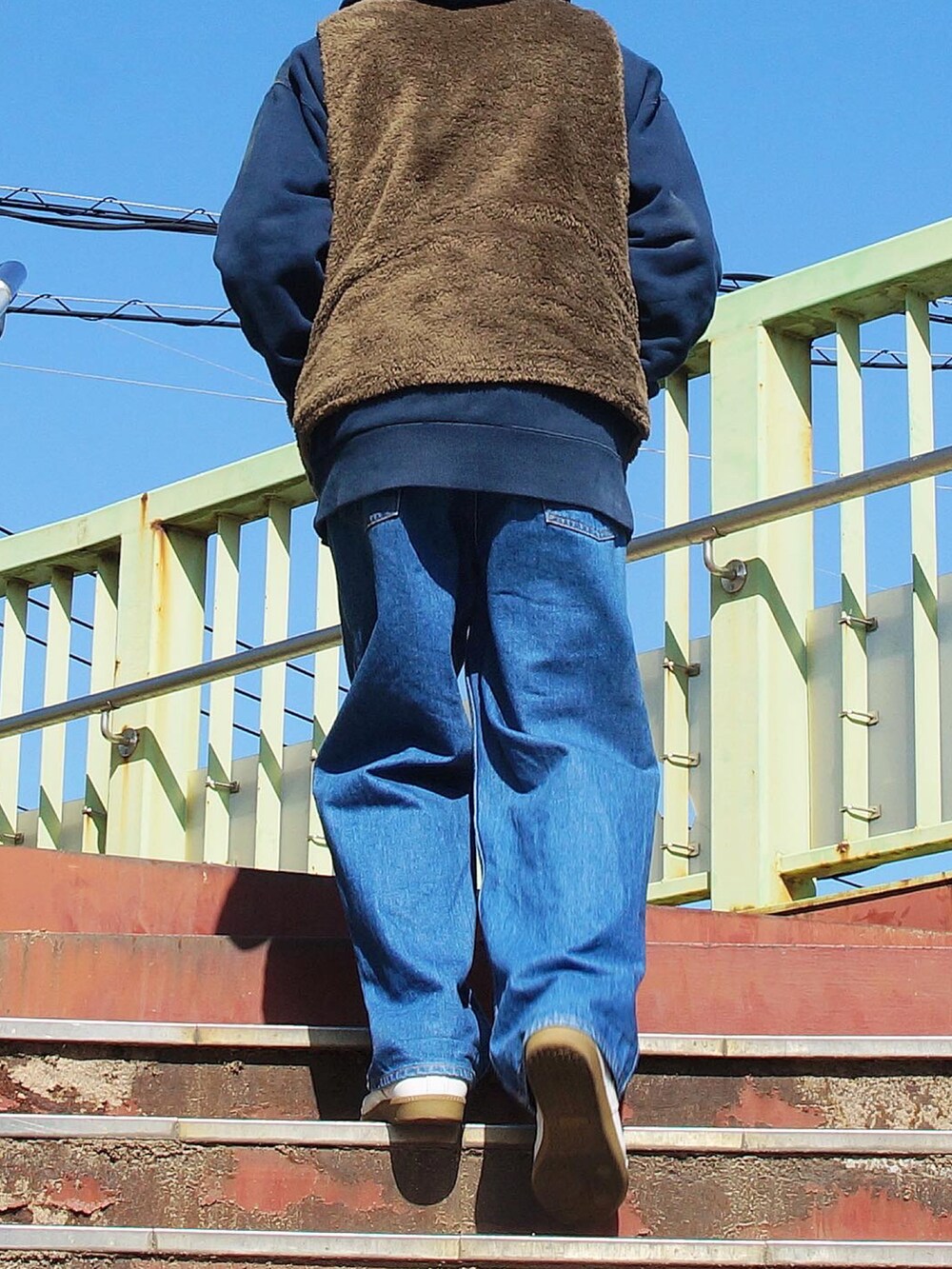 グリーン系のベスト、ブルー系のデニムパンツ、ホワイト系のスニーカーを着用したメンズの春コーディネートの2枚目の写真